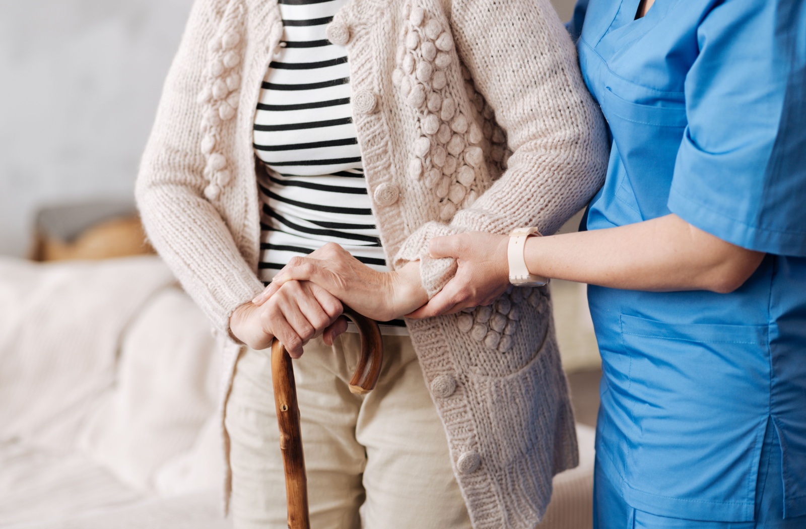 An older woman is being assisted by her nurse to help her walk with a cane.