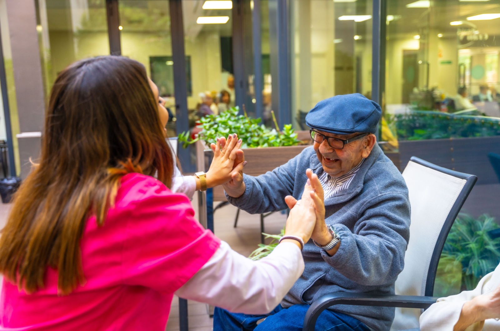 A smiling skilled nurse and a smiling resident sitting outside in a courtyard high-fiving each other.