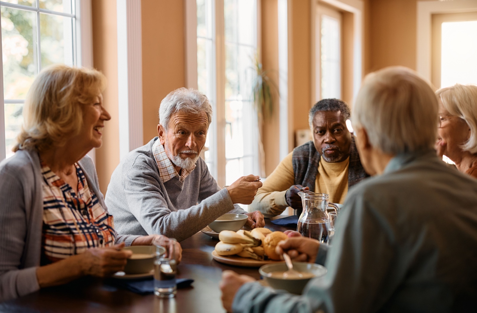 A group of seniors enjoying a meal together and chatting at a senior living community.
