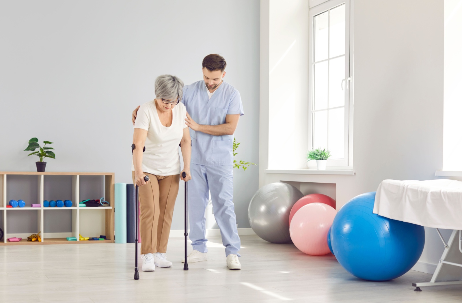 A nurse assists a senior patient walking with two canes during a physiotherapy session in a skilled nursing center.