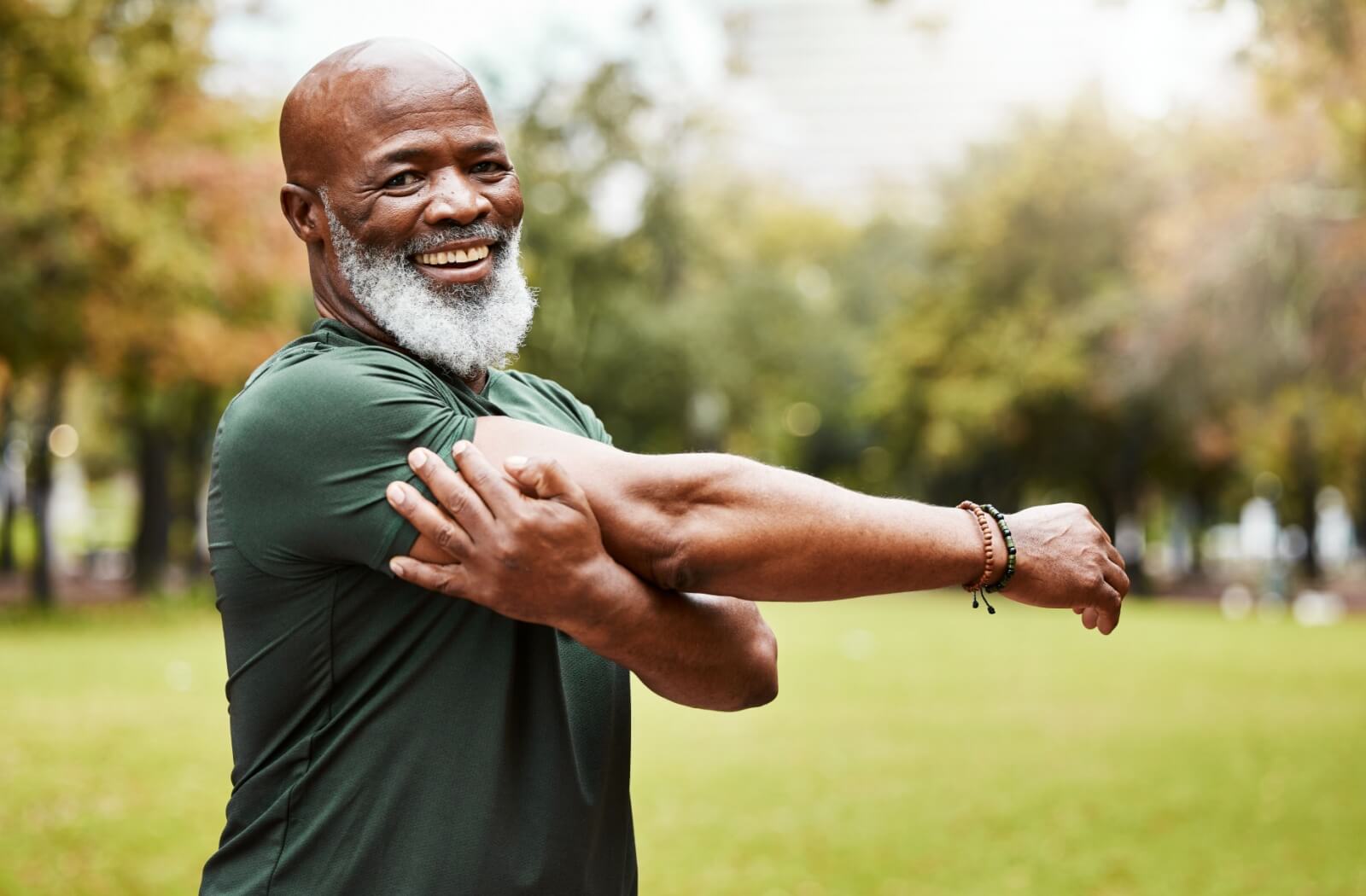 A senior stretching their arm and shoulder while smiling in the park.
