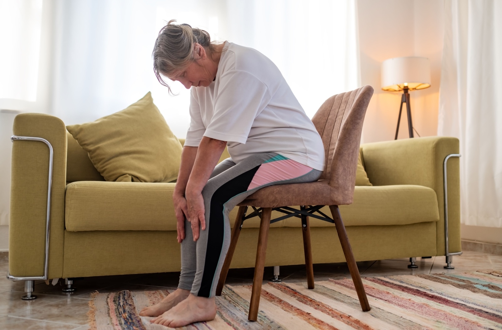 An older adult sitting with their head bowed in their living room while trying chair yoga.