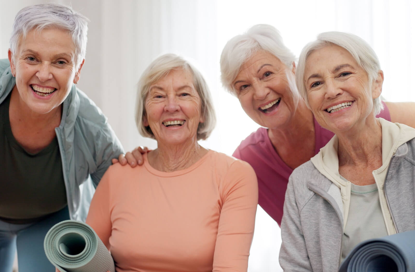 4 older adults holding rolled-up yoga mats smile at the camera after an exercise class