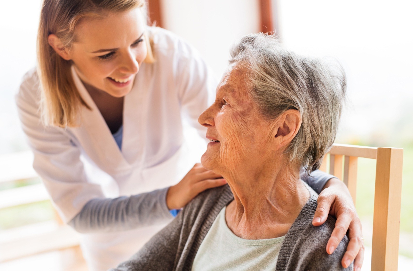 A respite care caregiver smiles at a sitting senior resident