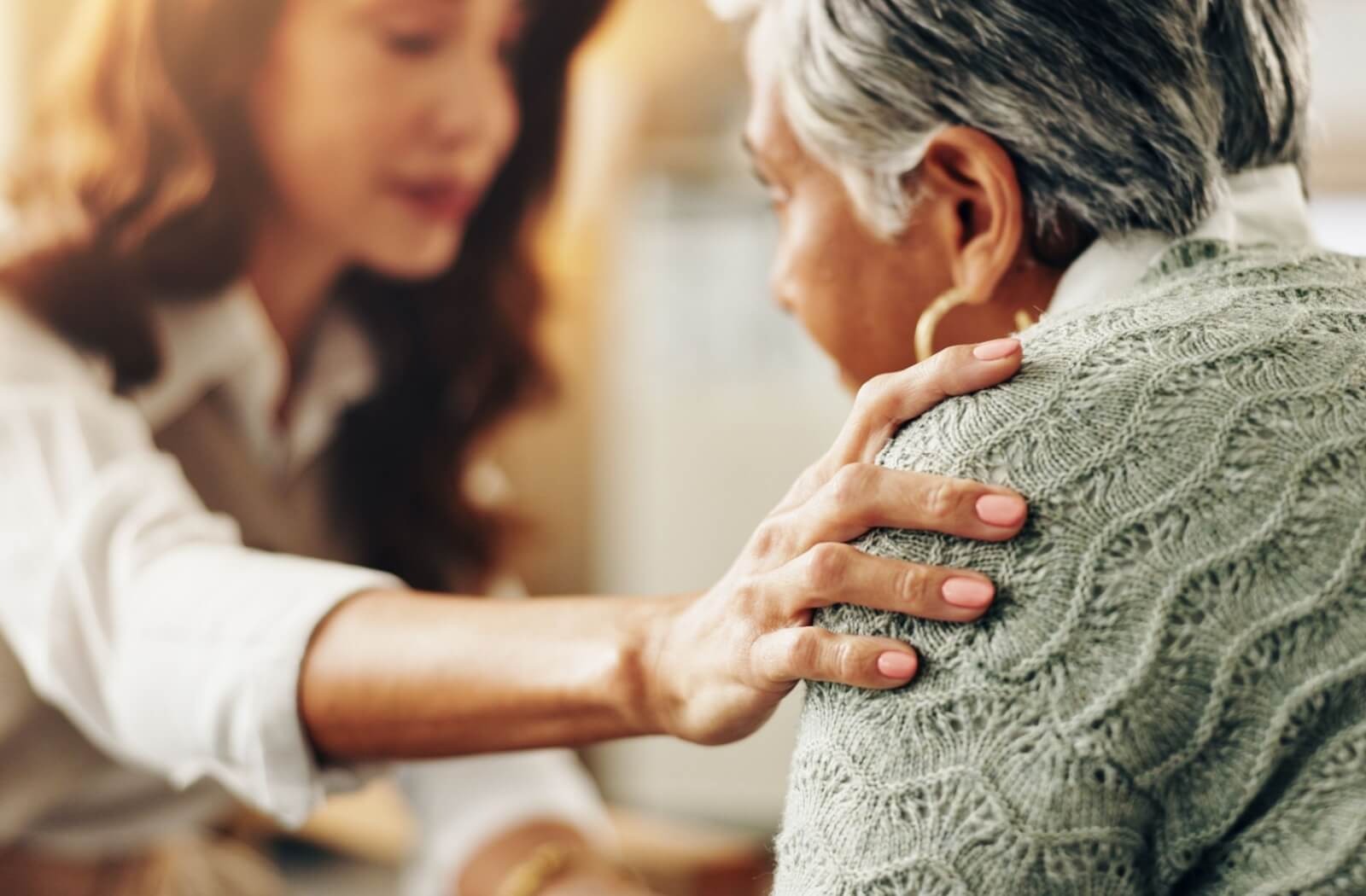 A caregiver in senior living gently touches a resident's shoulder to reassure them about their post-surgery mental health problems
