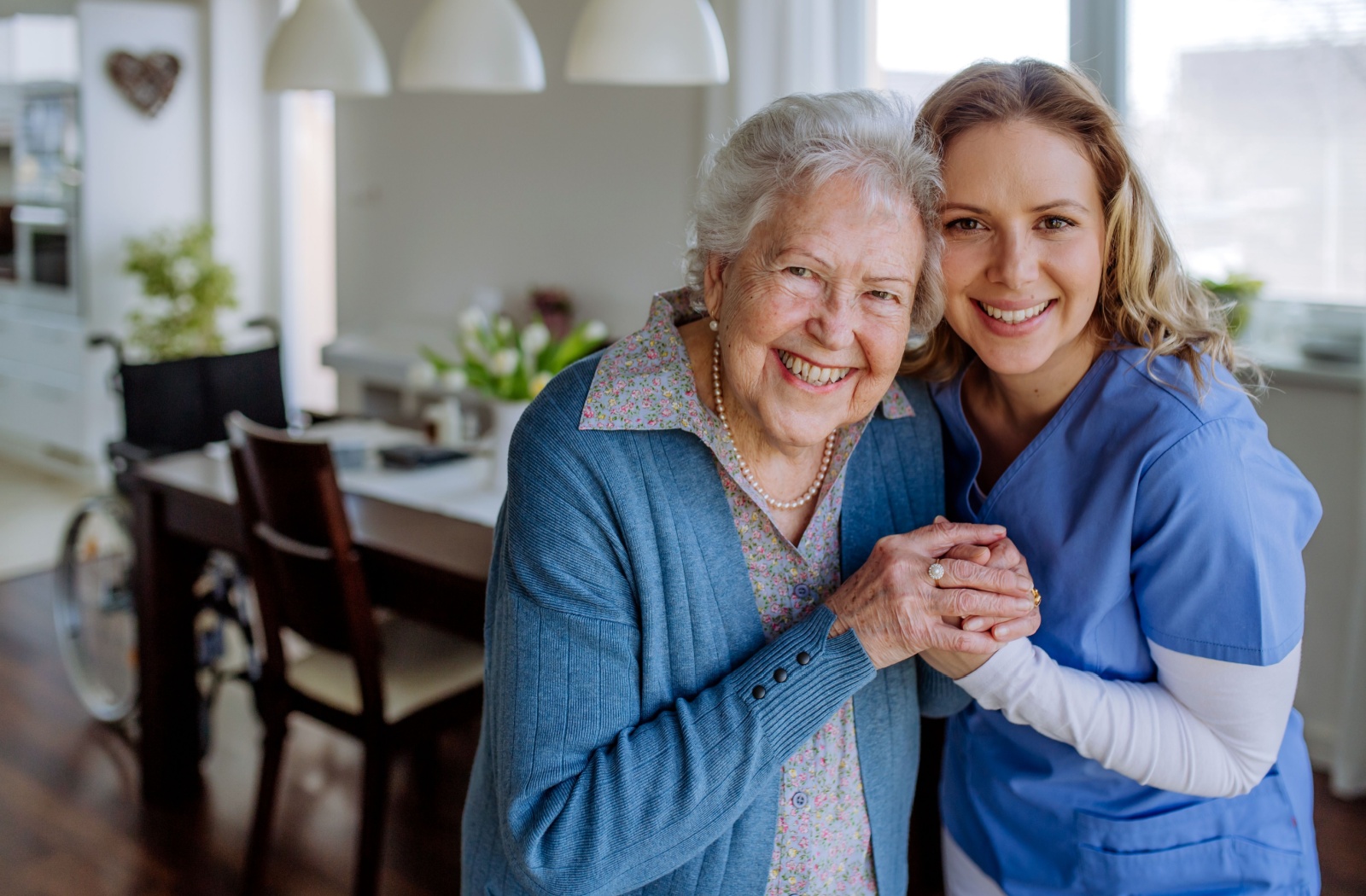 A respite caregiver and a senior hold hands and smile toward the camera.